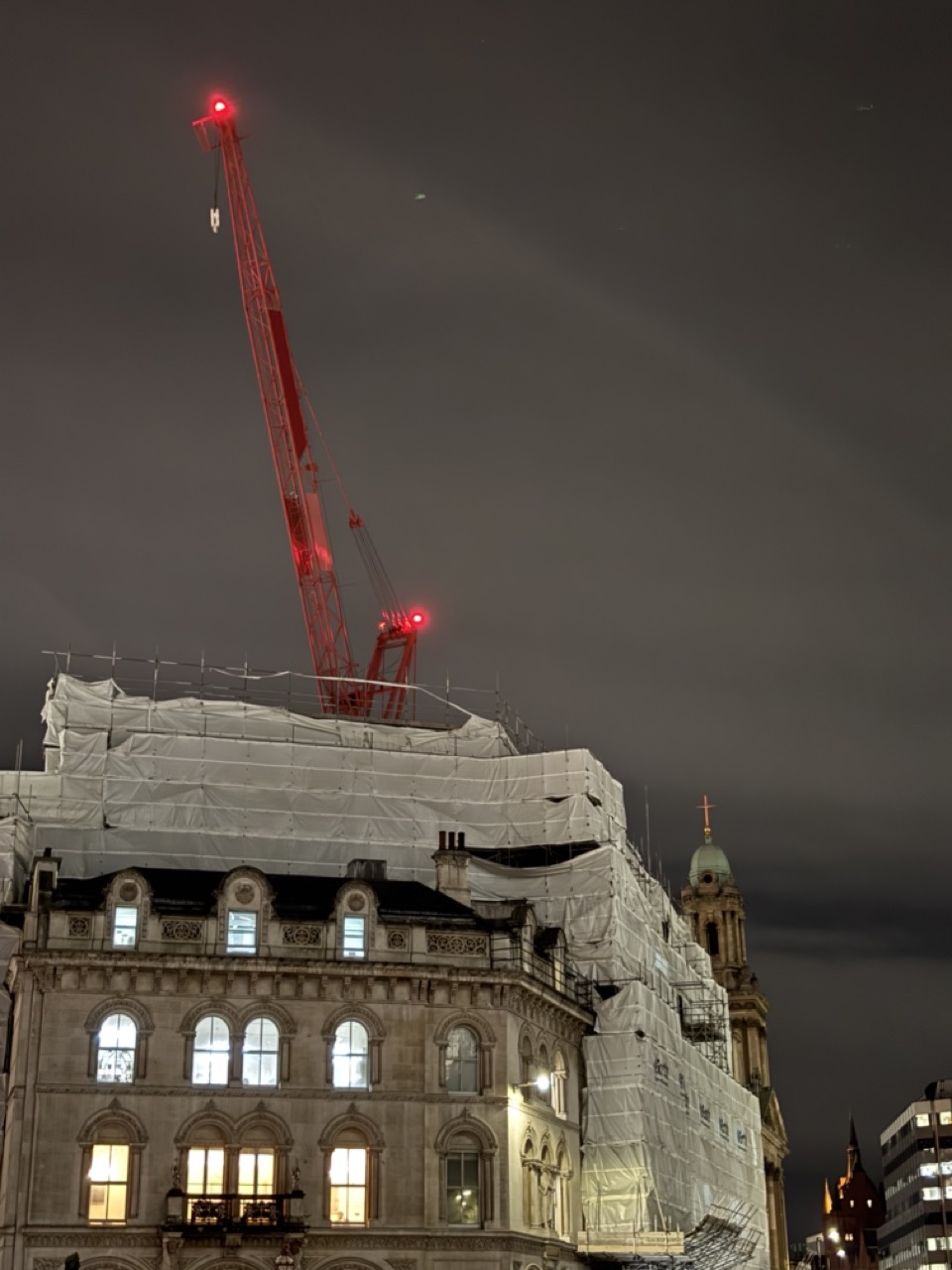 Photograph of building partially covered in scaffolding and polythene sheet. A large red crane is shown in the background. Holborn, London